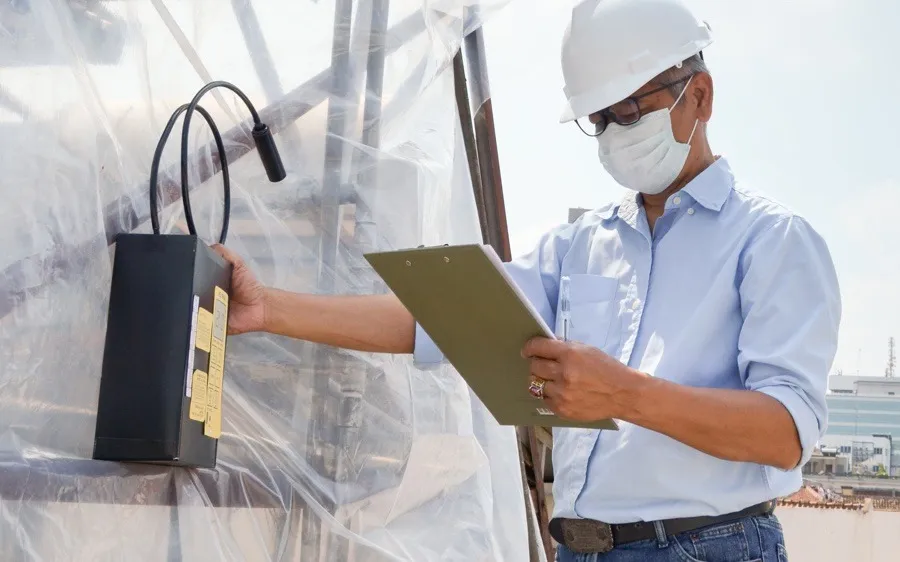 Hazid assessor running an air-sampling pump beside an enclosed work area on-site