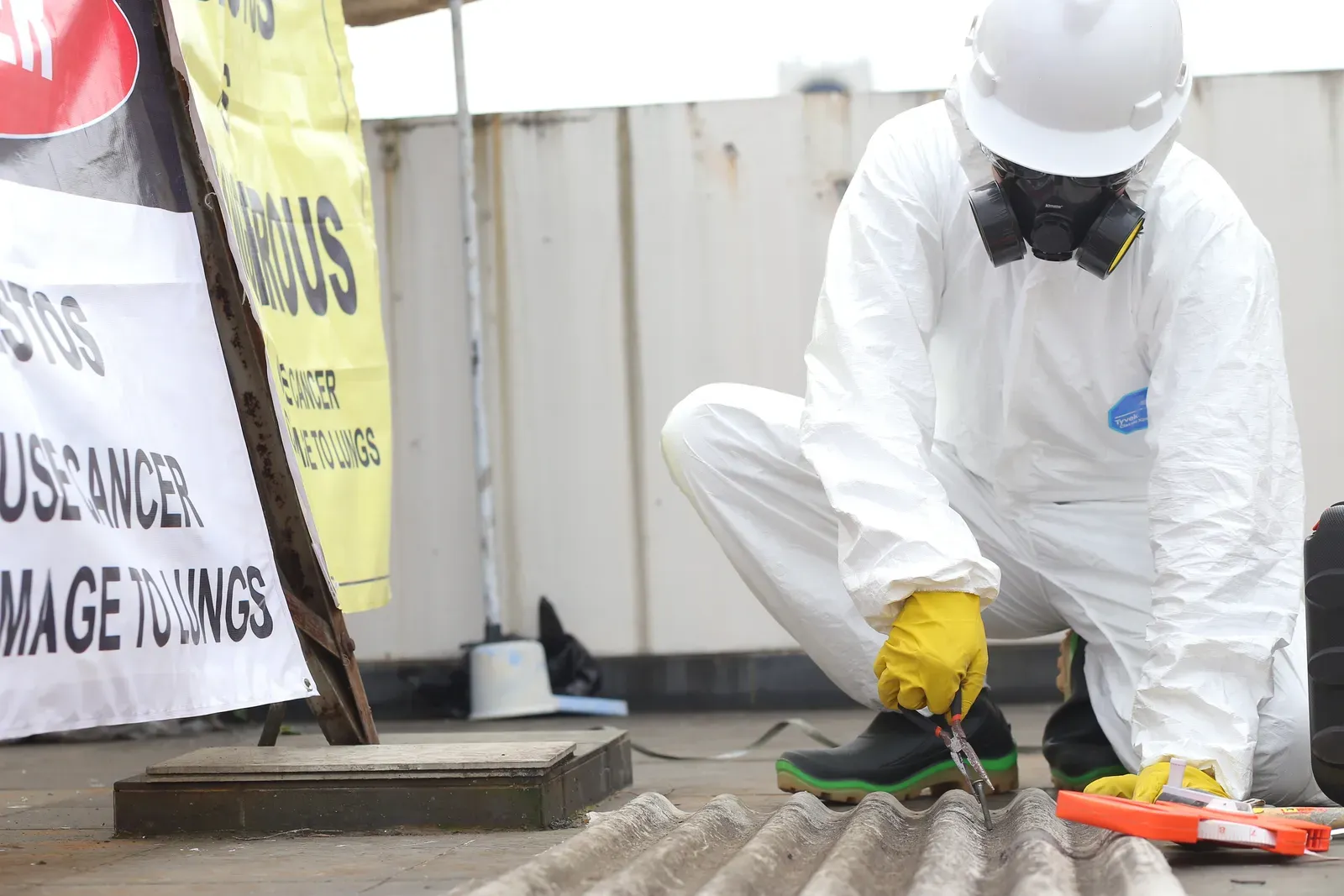 Licensed worker in PPE removing asbestos roof sheeting